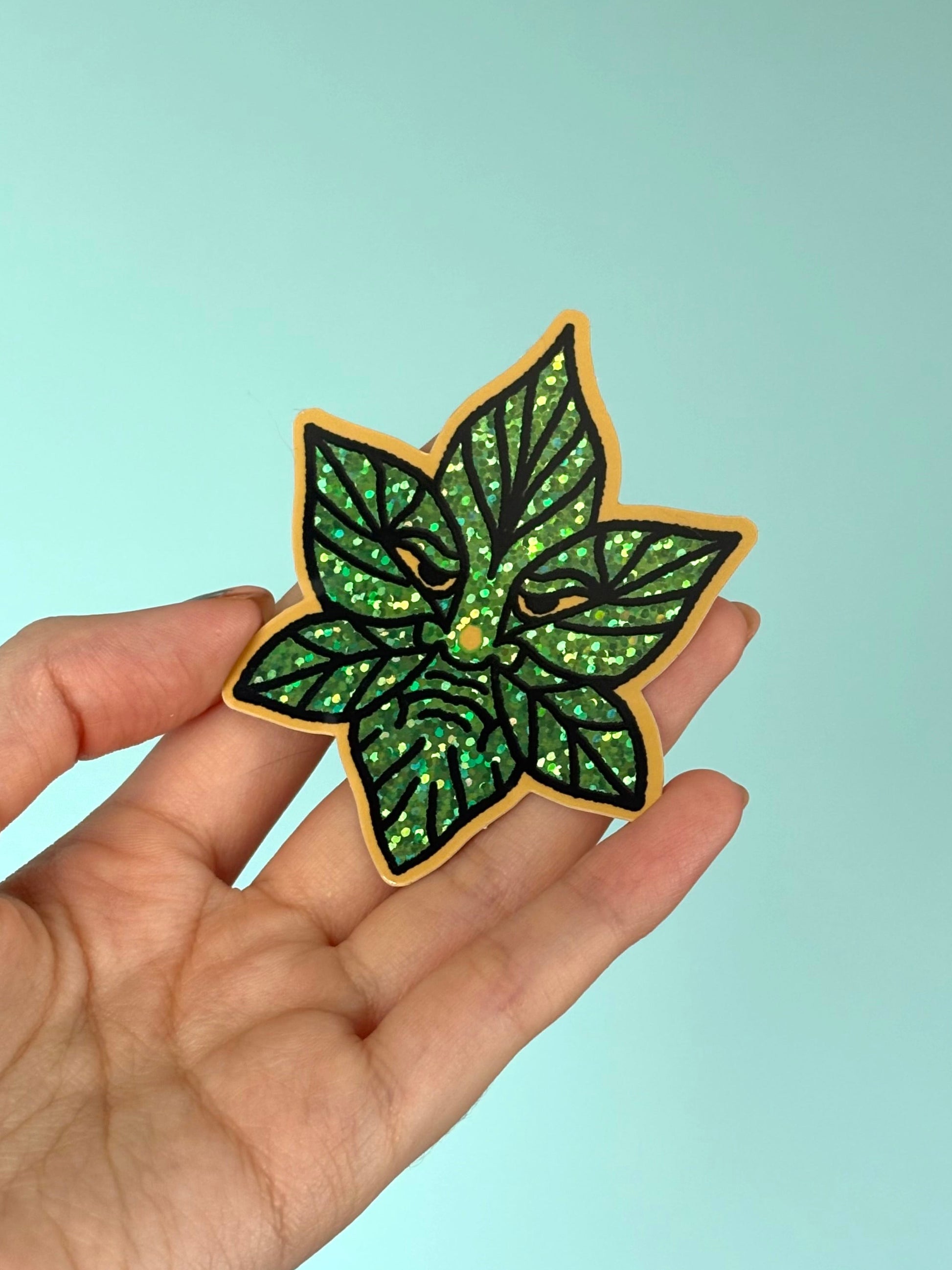 Hand holding a green leaf-shaped sticker against a light blue background
